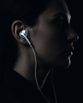 Silver earphone worn in ear, dark editorial portrait